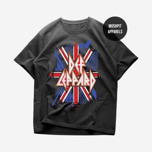 May include: A black short-sleeve t-shirt featuring a graphic print of the Def Leppard logo in white and orange, layered over a stylized Union Jack flag design in red, white, and blue. A circular black badge with the text MOSHPIT APPARELS is visible.