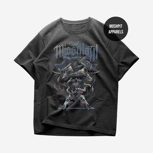 May include: A charcoal gray short-sleeve t-shirt featuring a graphic print with the text "MissMay!" above a central design of a skull, hands, and a snake. The artwork includes blue and white accents, geometric lines, and a black circular logo.