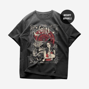 Puede incluir: Una camiseta gris carbón de manga corta con un estampado gráfico que incluye el texto GOJIRA en la parte superior. El diseño muestra un búho, una persona sosteniendo un conejo y un patrón circular rojo enmarcado por bordes ornamentados. Se observa un círculo negro con el texto MOSHPIT APPARELS.