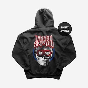 Pode incluir: Um moletom preto com capuz apresentando um gráfico nas costas com o texto Lynyrd Skynyrd acima de um crânio usando óculos vermelhos que dizem Free Bird. Um círculo azul envolve o crânio e um logotipo circular diz Moshpit Apparels.