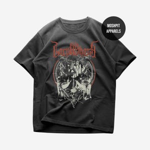 Peut inclure: Un t-shirt gris anthracite à manches courtes avec une impression graphique représentant une silhouette avec une couronne d'épines et un crâne. Le texte "BORNASHORD" est écrit en rouge au-dessus, avec un logo "MOSH PIT APPARELS" en haut à droite.