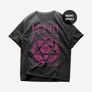 May include: A charcoal gray short-sleeve t-shirt featuring a pink graphic print. The design includes the text "HIM" above a circular emblem containing five roses arranged in a pentagram shape, surrounded by ornate decorative corner flourishes.