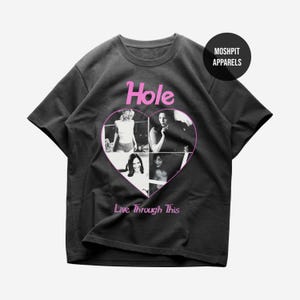 May include: A charcoal gray short-sleeve t-shirt featuring a pink heart graphic containing four black and white photographs. The text "Hole" appears above the heart, and "Live Through This" appears below. A "MOSH PIT APPARELS" logo is in the corner.