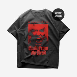 Puede incluir: Una camiseta negra de manga corta con un estampado gráfico rojo de un rostro con la boca abierta. El texto "HALESTORM" aparece sobre el gráfico y "BACK FROM THE DEAD" está impreso debajo en una fuente gótica. Se ve un logotipo circular "MOSH PIT APPARELS".