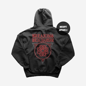 Può includere: Una felpa con cappuccio nera con una grafica rossa sul retro. Il design include il testo BREAKING BENJAMIN in un carattere stilizzato sopra un emblema a nodo circolare racchiuso in un triangolo. Un piccolo cerchio nero contiene MOSHPIT APPARELS.