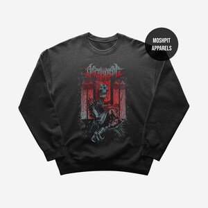 Könnte beinhalten: Ein schwarzes Sweatshirt mit Rundhalsausschnitt und einem Grafikdruck einer skelettierten Figur in einer rot-grauen Umgebung. Der Text "ARCHSPIRE" steht über der Figur, und ein kreisförmiges Abzeichen oben rechts zeigt "MOSH PIT APPARELS".