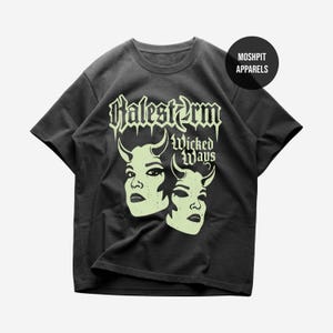 Puede incluir: Una camiseta gris carbón de manga corta con un gráfico verde pálido de dos rostros con cuernos. El texto dice Halestorm y Wicked Ways en una fuente gótica. Un logotipo negro circular en la esquina superior derecha muestra MOSHPIT APPARELS.