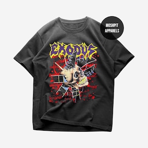 May include: A charcoal gray short-sleeve t-shirt featuring a graphic print of a skull with yellow teeth, red paint splatters, and geometric shapes. The word EXODUS is printed in yellow and purple above the skull, with MOSHPIT APPARELS in a circle.