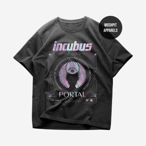 May include: A charcoal gray short-sleeve t-shirt featuring a graphic print with the text "incubus" and "PORTAL" in a gradient iridescent color. The design includes a circular pattern, starburst accents, and the text "PARTNERSHIP OF RESPONSIBLE TRIPPERS ADVOCATING FOR LEGALIZATION".
