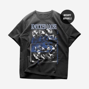 May include: A charcoal grey short-sleeve t-shirt featuring a graphic print with the text KNOCKED LOOSE at the top and A DIFFERENT SHADE OF BLUE on the side. The design includes abstract blue and white imagery with a circular MOSHPIT APPARELS logo.