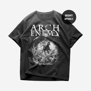 May include: A black short-sleeve t-shirt featuring a white graphic print of a figure on horseback, a skull, and the text ARCH ENEMY and My Apocalypse. A circular black badge in the upper right corner displays the text MOSHPIT APPARELS in white.