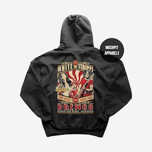 May include: A black hooded sweatshirt featuring a graphic on the back with the text The White Stripes, Our Beers Will Rock You, and Brewco Manhattan Beach, California. The illustration depicts a drummer and a guitarist with red sunburst rays.