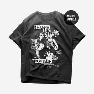 Könnte beinhalten: Ein anthrazitfarbenes Kurzarm-T-Shirt mit einem weißen Grafikdruck der Band Måneskin. Das Design enthält den Text I WANNA BE YOUR SLAVE, Liedtexte und den Albumtitel TEATRO D'IRA. Ein kreisförmiges MOSHPIT APPARELS-Logo befindet sich oben rechts.