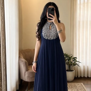 May include: A navy blue sleeveless tunic featuring a high halter neckline with a keyhole cutout and intricate silver embroidery around the collar, paired with matching wide-leg trousers in a solid navy blue fabric with a pleated skirt overlay.