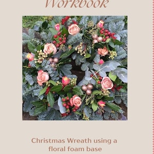 May include: A workbook titled Flower Fiestas Workbook featuring a central image of a Christmas wreath made with blue-green pine needles, pink roses, red berries, and small glittery gold spheres, with text below reading Christmas Wreath using a floral foam base.
