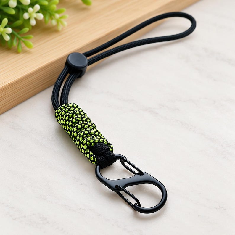 Puede incluir: Un cord&oacute;n de paracord negro y verde ne&oacute;n con una secci&oacute;n trenzada, un cierre de pl&aacute;stico negro y un mosquet&oacute;n de metal negro. El cord&oacute;n est&aacute; fabricado con hilos de nailon tejidos, lo que proporciona un lazo resistente para sujeci&oacute;n.
