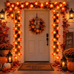 Puede incluir: Una puerta de entrada decorada para el otoño con una corona de calabazas, piñas y hojas, enmarcada por guirnaldas de hojas de arce iluminadas. Dos faroles negros, crisantemos naranjas y calabazas decoran el porche con un felpudo.