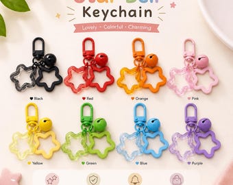 May include: A collection of eight star-shaped keychains in black, red, orange, pink, yellow, green, blue, and purple. Each keychain features a lobster clasp, a small bell, and two open star charms in matching colors. The text Star Bell Keychain is visible.