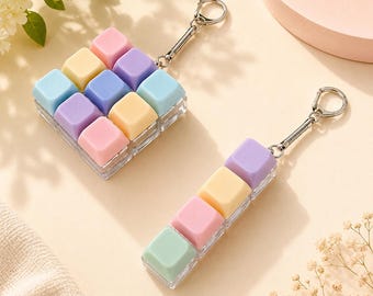 May include: Two keychains featuring pastel-colored square keycaps arranged in grids. One keychain has a three-by-three square grid of nine keycaps in pink, yellow, blue, and purple. The other is a single row of four keycaps in green, pink, yellow, and purple.