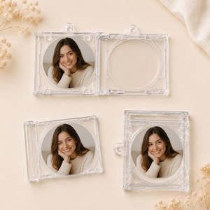 Könnte beinhalten: Drei quadratische, transparente Acrylrahmen mit Aufhängeösen, die jeweils ein kreisförmiges Foto einer lächelnden Person mit langem braunem Haar in einem cremefarbenen Pullover enthalten. Ein Rahmen ist leer und zeigt einen runden Ausschnitt.