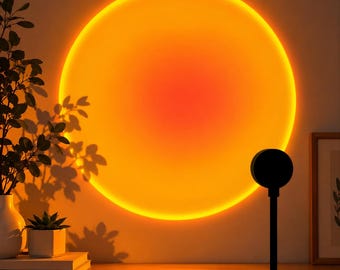 Puede incluir: Una lámpara de proyección de atardecer con un cabezal circular negro y un soporte delgado, que proyecta una gran luz circular de color naranja y amarillo vibrante sobre la pared. La luz crea un brillo cálido que ilumina el área y las plantas.