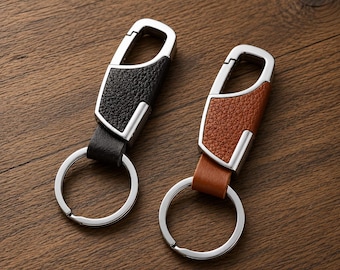 May include: Two keychains featuring a silver-toned metal carabiner clip with a textured leather insert. One keychain has a black leather inlay, while the other has a tan leather inlay. Each includes a circular metal split ring for holding keys.