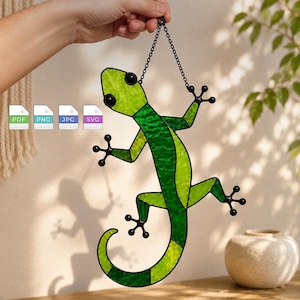 May include: A stained glass gecko suncatcher featuring vibrant lime and forest green textured glass panels outlined in black metal. The lizard-shaped ornament hangs from a black metal chain and includes digital file icons labeled PDF, PNG, JPG, and SVG.