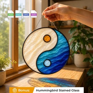 Puede incluir: Un atrapasoles circular de vidrieras con un diseño de yin-yang, con un lado texturizado de color crema y un lado texturizado azul. El lado crema contiene un pequeño círculo naranja y el lado azul contiene un pequeño círculo azul claro.