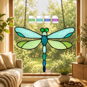 May include: A stained glass dragonfly suncatcher featuring teal and light green wings with a segmented body in shades of blue and green. The piece hangs from a black metal chain and includes four small icons labeled PDF, PNG, JPG, and SVG.