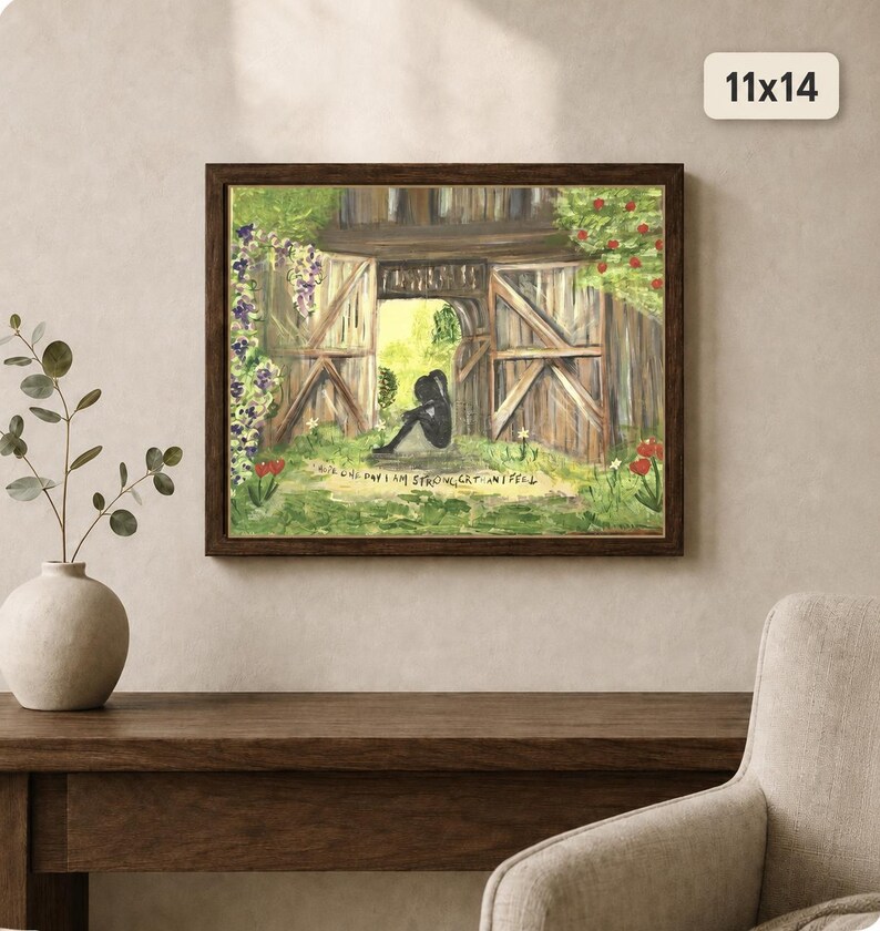 K&ouml;nnte beinhalten: Ein gerahmtes 28x36 cm Gem&auml;lde, das die Silhouette einer Person in einem offenen Scheunentor aus Holz zeigt. Die Szene umfasst gr&uuml;nes Gras, rote und violette Blumen sowie den Text "I HOPE ONE DAY I AM STRONGER THAN I FEEL" unter der Figur.