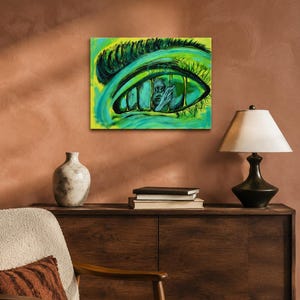 May include: A rectangular canvas painting featuring a large, stylized human eye rendered in vibrant shades of lime green and teal. The iris contains a dark, detailed illustration of a figure trapped behind vertical bars, set against a bright background.