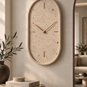 May include: An oval wall clock with a textured beige stone face featuring natural porous markings. The clock has thin, straight gold-toned metal hands and simple gold-toned hour markers at the twelve, three, six, and nine o'clock positions.