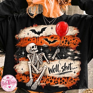 May include: A black long-sleeve sweatshirt featuring a graphic print of a skeleton sitting and holding a red balloon. The design includes orange and black leopard print stripes, black bats, a spider web, and the text "Well, shit..." in black.