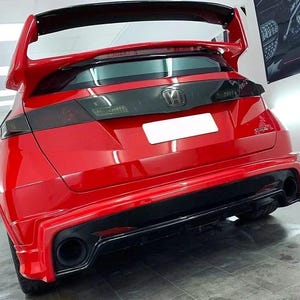 Può includere: Una hatchback Honda Civic Type R rosso brillante vista dal retro. Il veicolo presenta un prominente spoiler posteriore nero, luci posteriori oscurate, un diffusore del paraurti posteriore nero con doppio scarico e un emblema Honda argentato.