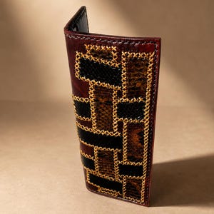 May include: A vertical leather wallet featuring a dark burgundy base with an intricate patchwork design of black and brown snakeskin-textured panels. The panels are joined together by prominent, decorative gold-coloured cross-stitching.
