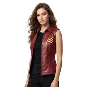 May include: A sleeveless dark red leather vest featuring a classic collar, a full-length front zipper, and a gold-colored embroidered wing-shaped emblem on the left chest. The garment is worn over a simple black top and black trousers.