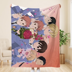May include: A soft fleece blanket featuring a colorful anime-style illustration of seven characters in blue school uniforms. The group is surrounded by pink flower petals, with one character holding a bouquet of red roses and another a pink plush toy.