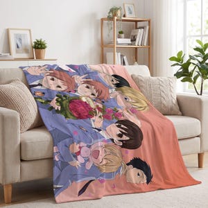 May include: A soft throw blanket featuring a colorful anime-style illustration of six characters in school uniforms. The design includes a bouquet of red roses, a small pink plush toy, and scattered pink petals against a soft peach background.