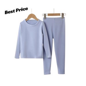 May include: A light blue long-sleeved top and matching leggings set hanging on wooden hangers. The text "Best Price" is visible in the upper left corner. The clothing set features a solid light blue colour, a crew neckline, and a simple design.