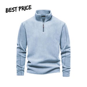Puede incluir: Un suéter de forro polar azul claro con cierre de cremallera de un cuarto, tirador plateado y cuello alto. La prenda incluye mangas largas con detalles de costuras visibles a lo largo de los brazos y el texto BEST PRICE.