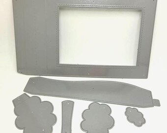 May include: A set of six silver-colored metal craft dies for paper cutting. The collection includes a large rectangular frame with a beaded border, a long curved strip, two cloud-shaped pieces, a small cloud, and a narrow vertical stem-like shape.