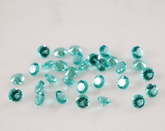 May include: A scattering of teal green round rhinestones on a white surface.