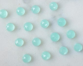 May include: A collection of 16 light blue gemstone beads, each with a faceted surface, arranged on a white marble background.