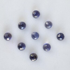 May include: Ten faceted, round, dark blue gemstones on a white surface.