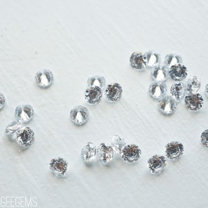 May include: A scattering of clear, round, faceted rhinestones on a white surface.