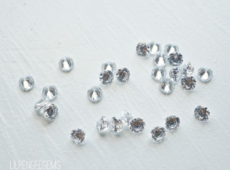 May include: A scattering of clear, round, faceted rhinestones on a white surface.
