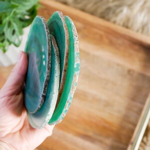 May include: A set of four green agate coasters with a natural, raw edge. The coasters are stacked on top of each other and are being held in a hand.