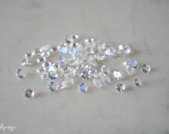 May include: A pile of iridescent clear gemstones, scattered on a white surface.