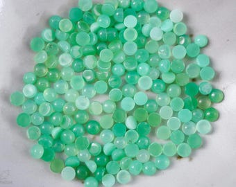 May include: A pile of green and white cabochon gemstones, also known as green opal, on a white surface.