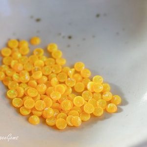 Puede incluir: Un montón de pequeños cabujones de ópalo amarillo redondos. Los cabujones son lisos y brillantes, con un ligero brillo iridiscente.